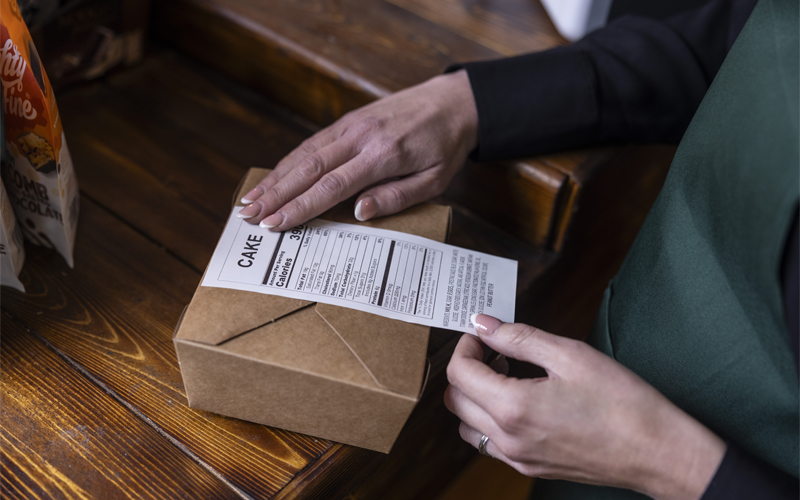 Woman in a green apron attaching a linerless label to a cardboard box
