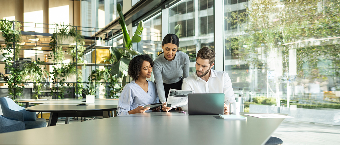 Two males and female sat working in a colourful office environment with one female stood by window using Brother printer