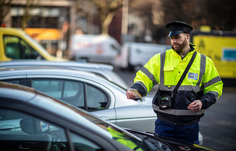 Parkeringsvagt, der lægger en parkeringsbøde på en bil